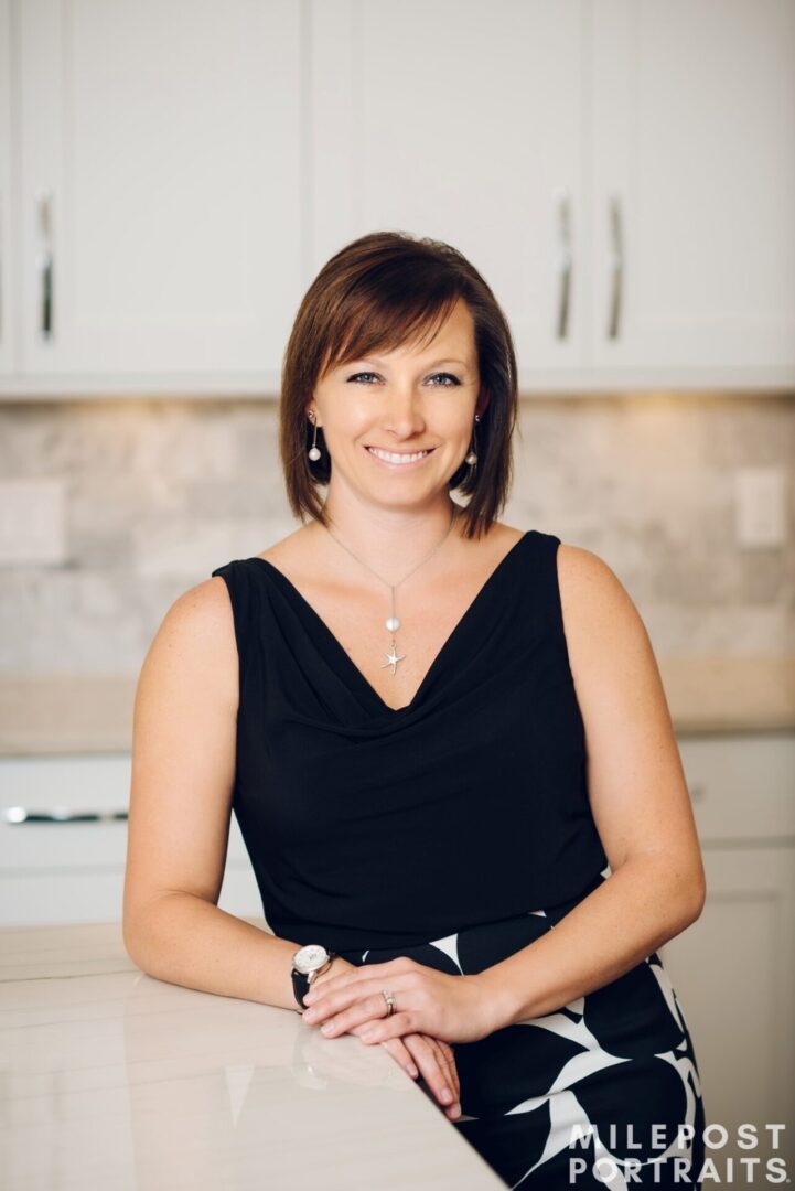 Woman smiling in a black sleeveless dress indoors.