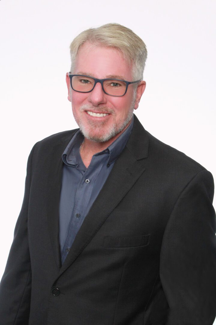 Smiling man in glasses and black blazer against white background.