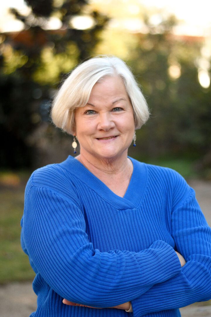 Smiling elderly woman with white hair wearing a blue sweater outdoors.