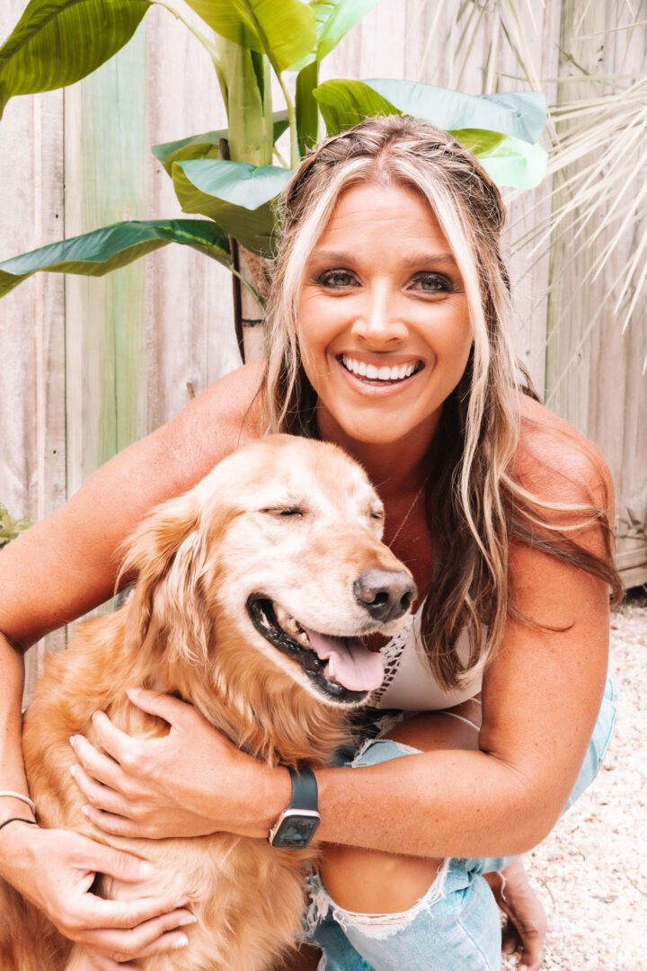 A smiling woman with long blonde hair hugs a happy golden retriever.