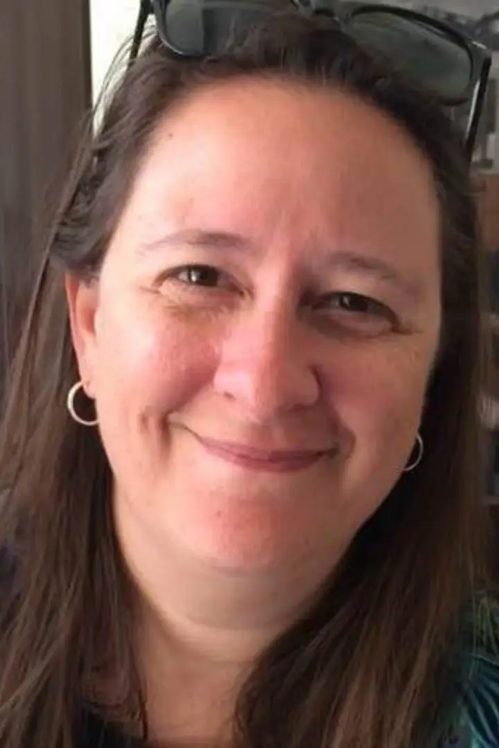 Close-up of a smiling woman with long brown hair and hoop earrings.