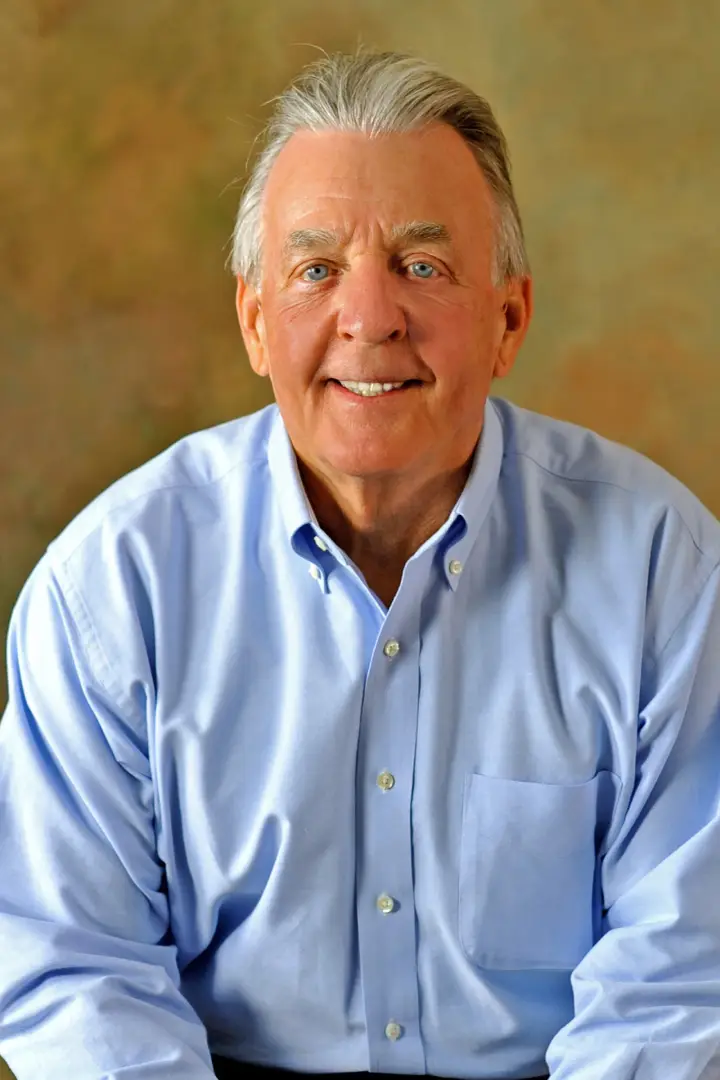 Smiling elderly man in a light blue shirt.