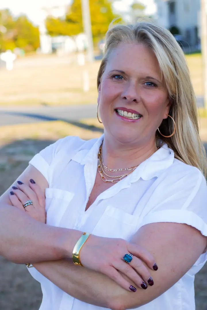 Smiling woman with crossed arms outdoors in casual white shirt.