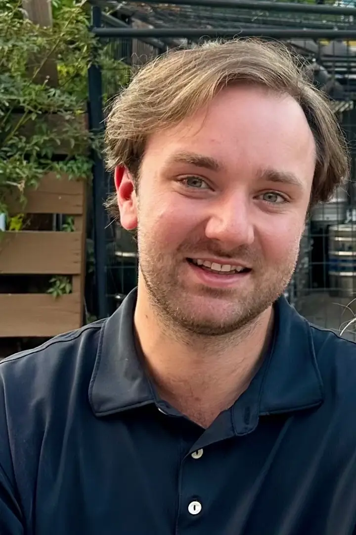 A smiling man with light brown hair in a dark polo shirt.