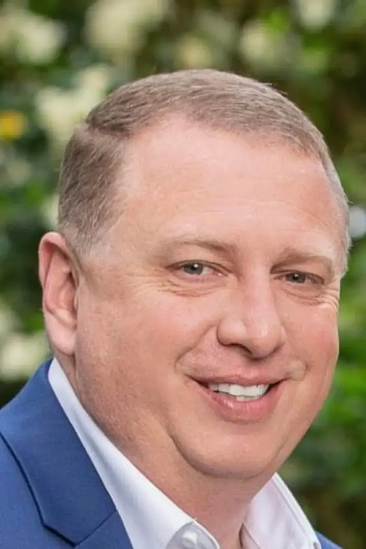 Close-up of a smiling man in a blue suit jacket.