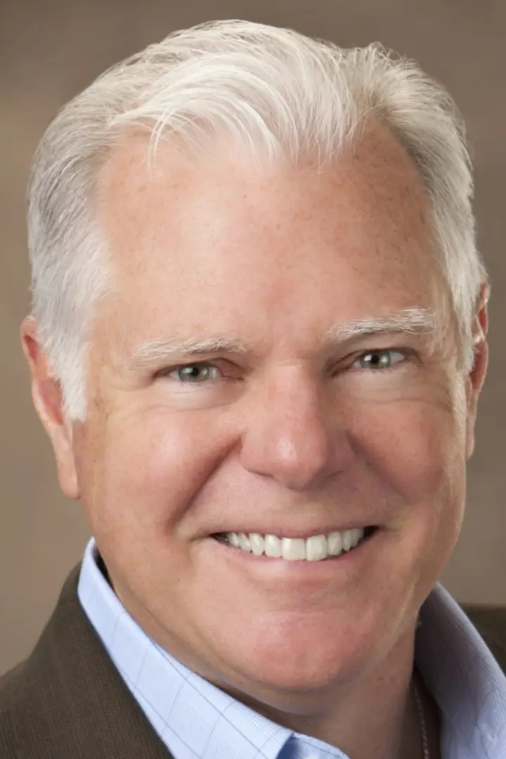 Close-up of a smiling older man with white hair and light eyes.