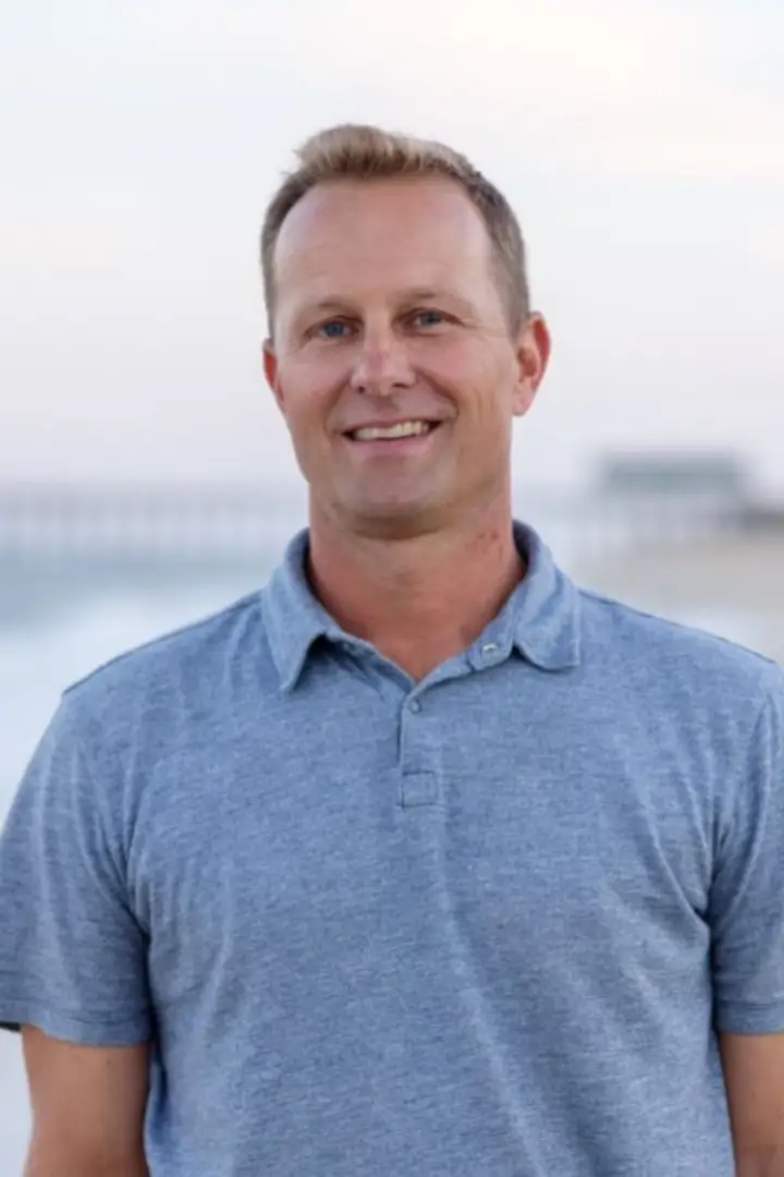 Smiling man in a blue polo shirt with a blurred outdoor background.