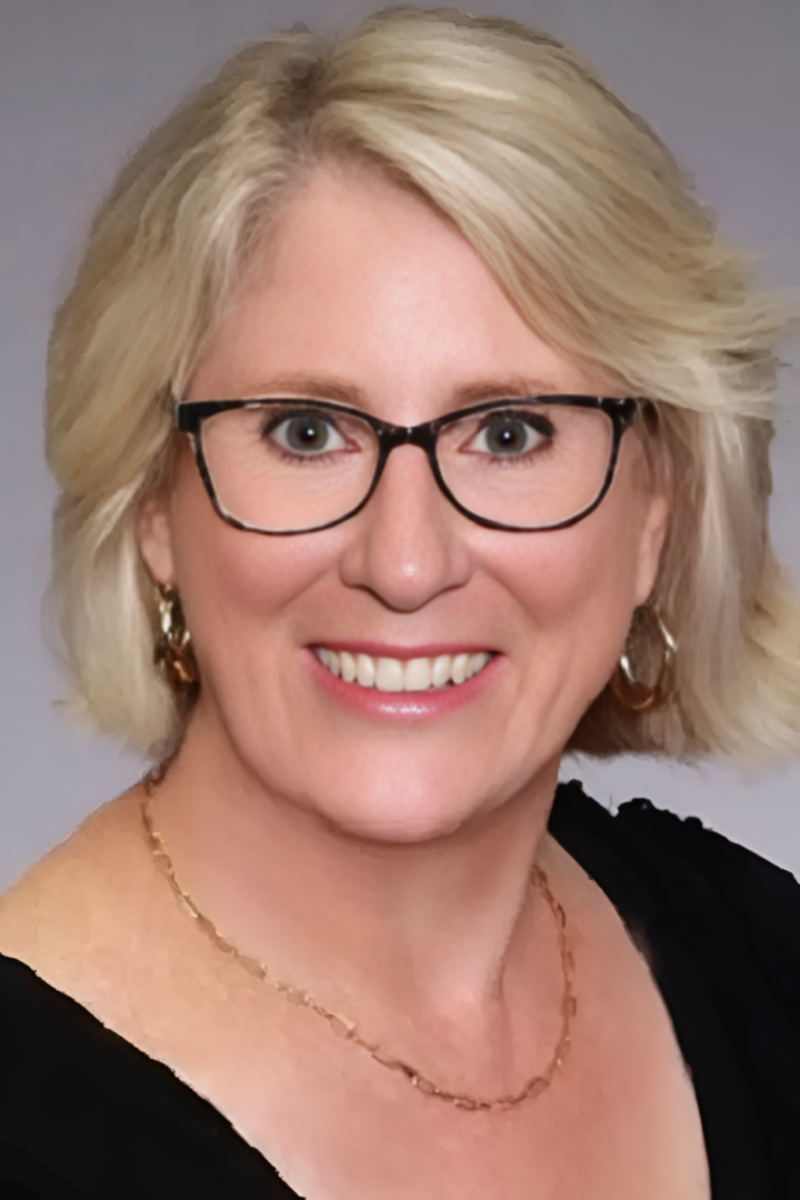 Smiling woman with glasses and short blonde hair.