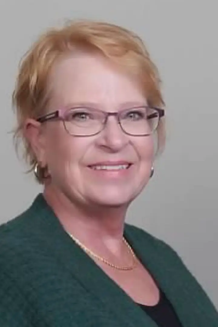 Smiling middle-aged woman with glasses and short blonde hair.