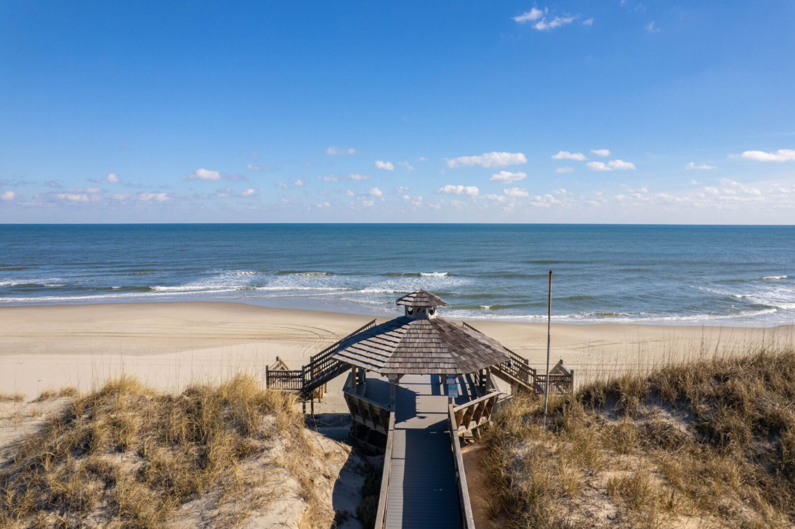 A wooden boardwalk leads to a beach with a pier extending into the ocean.