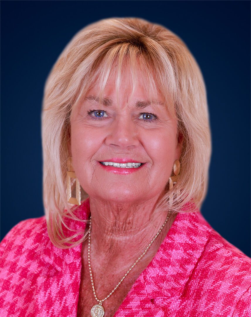 Smiling middle-aged woman with blonde hair and pink attire.